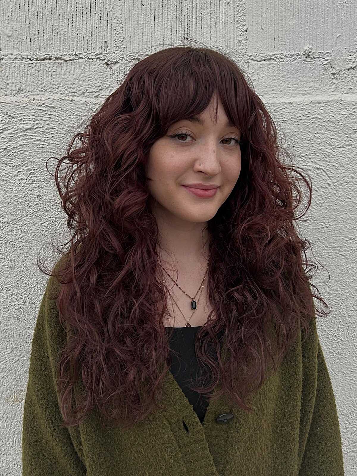 Long curly burgundy hair with layered curtain bangs