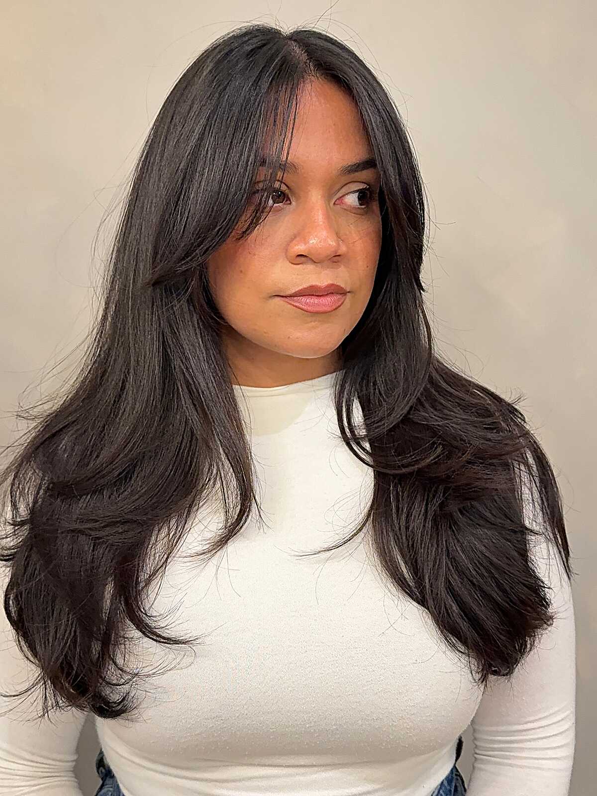 Dark long layered hair with wispy curtain bangs and flipped ends