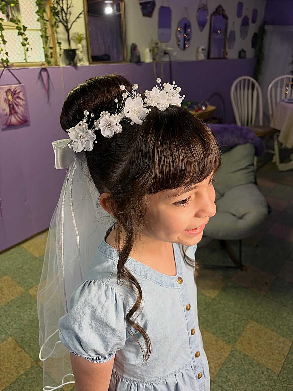 High bun with white floral crown, bangs, and trailing veil