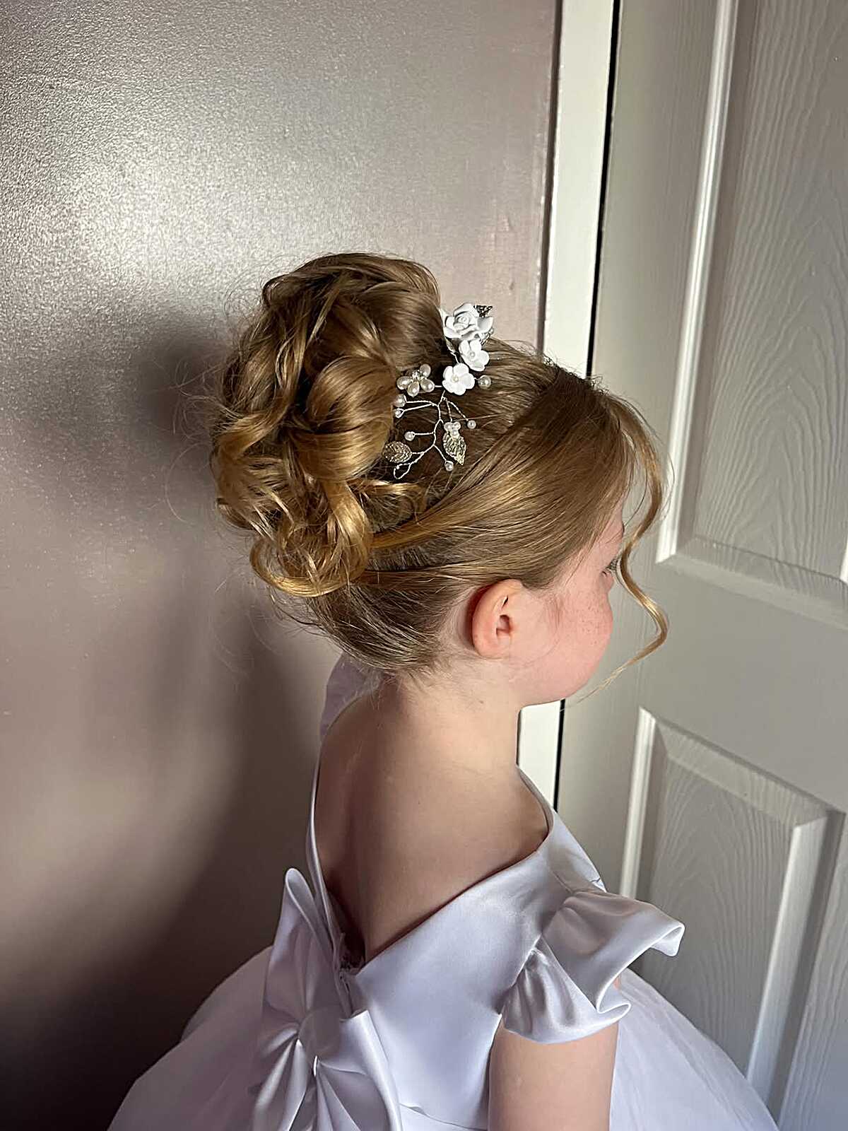 Tousled curly high updo with small floral pin on blonde hair
