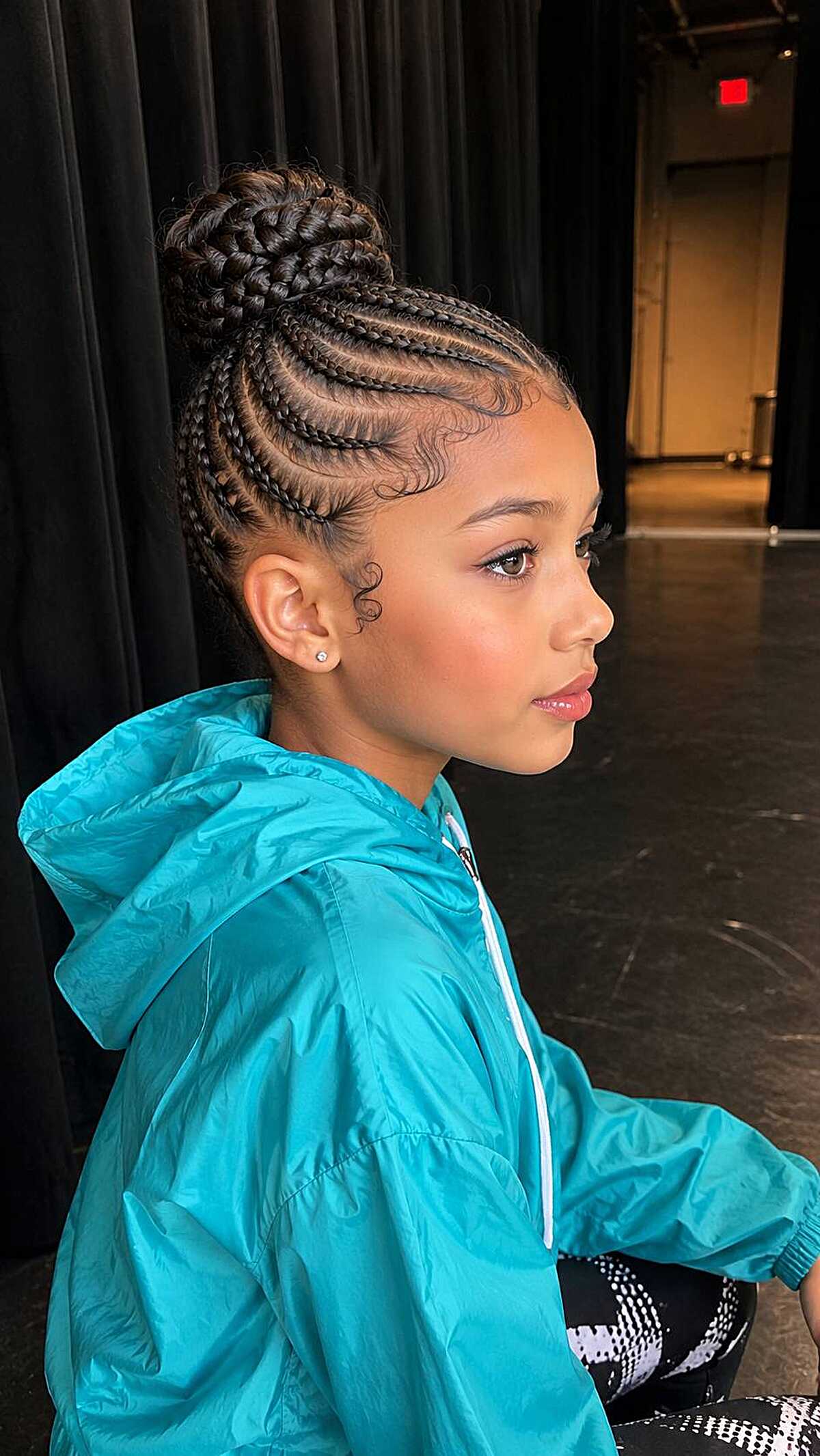 Girl with feed-in cornrow braids into a top knot bun