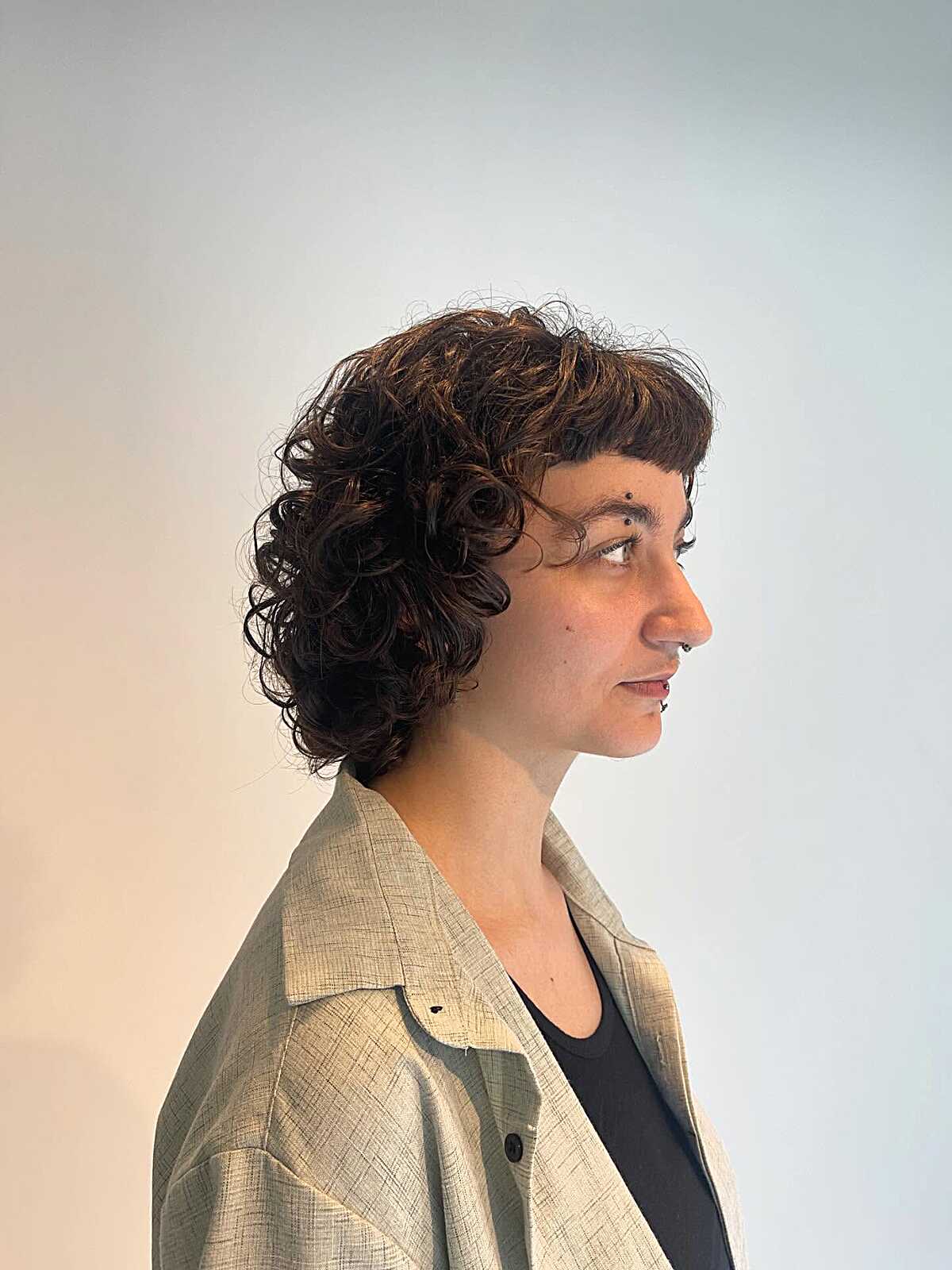 Dark curly bob with short micro bangs and side profile