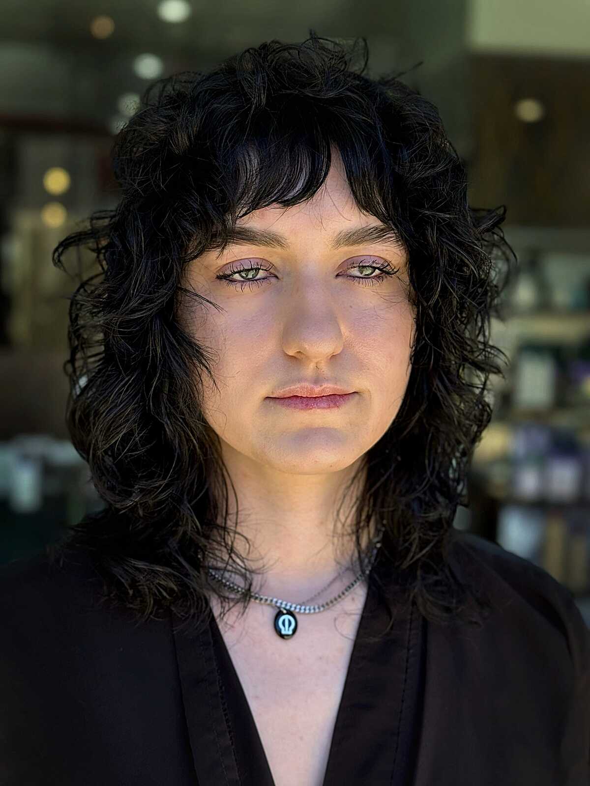 Dark curly shoulder-length mullet with bangs