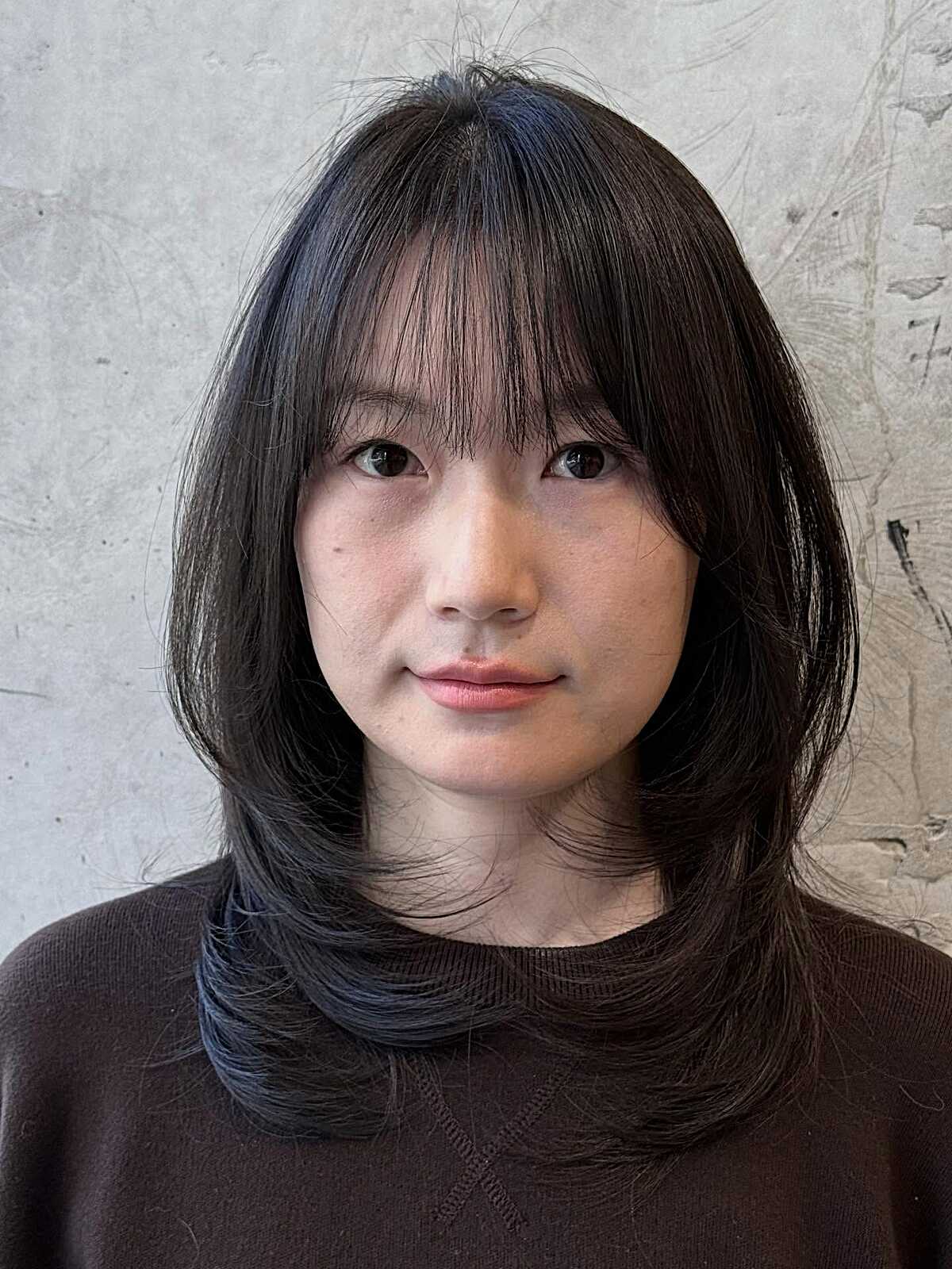 Dark mid-length hair with wispy bangs and soft layers