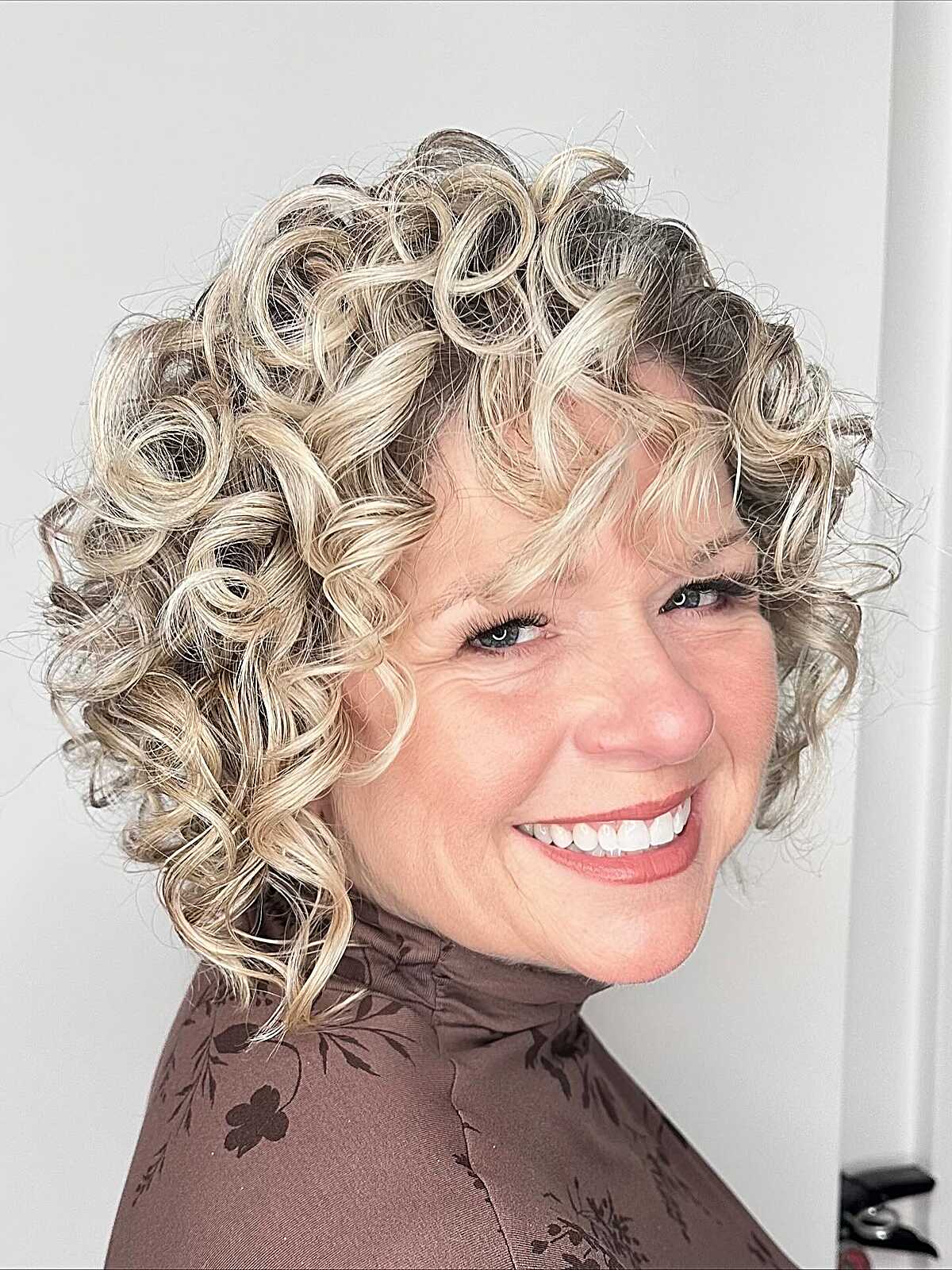 Voluminous blonde curly bob with dark roots and bangs