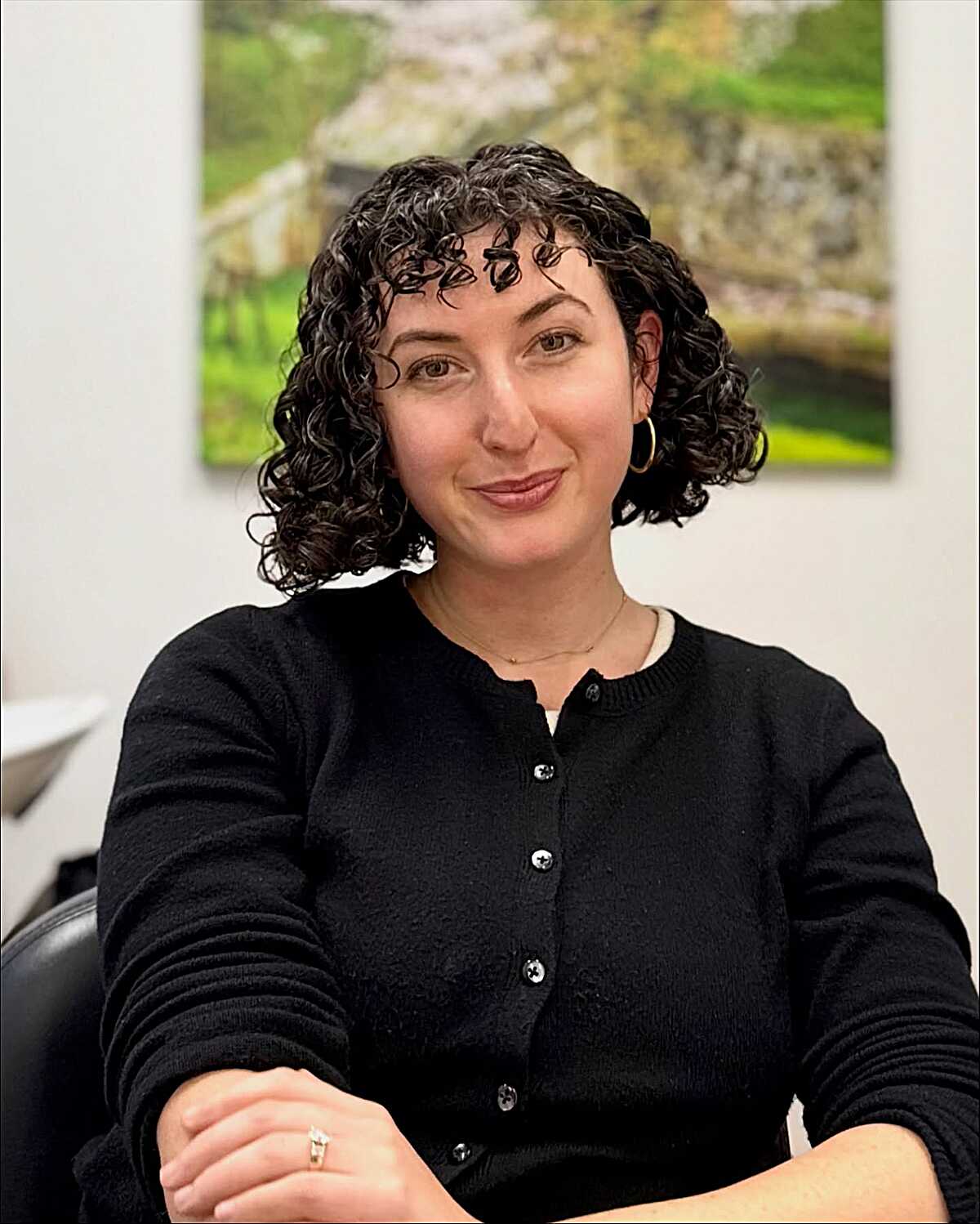 Defined dark curly bob with side part and small hoops