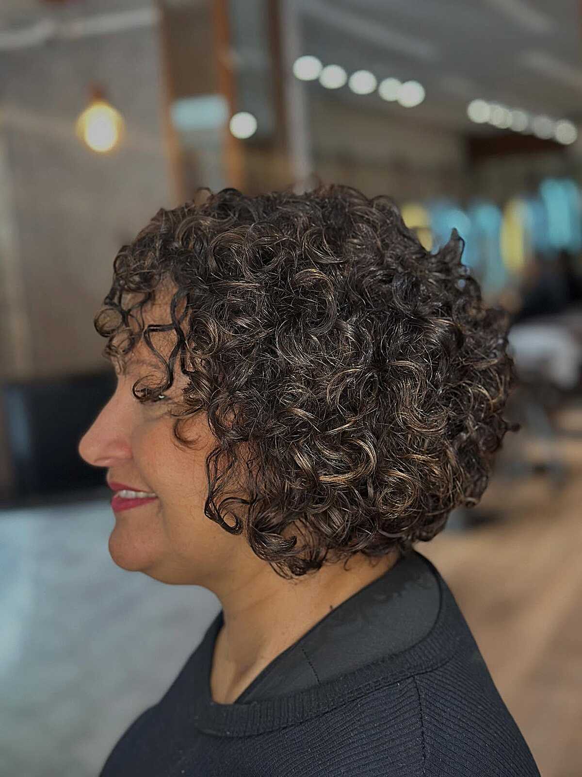 Profile of dark curly bob with subtle caramel highlights